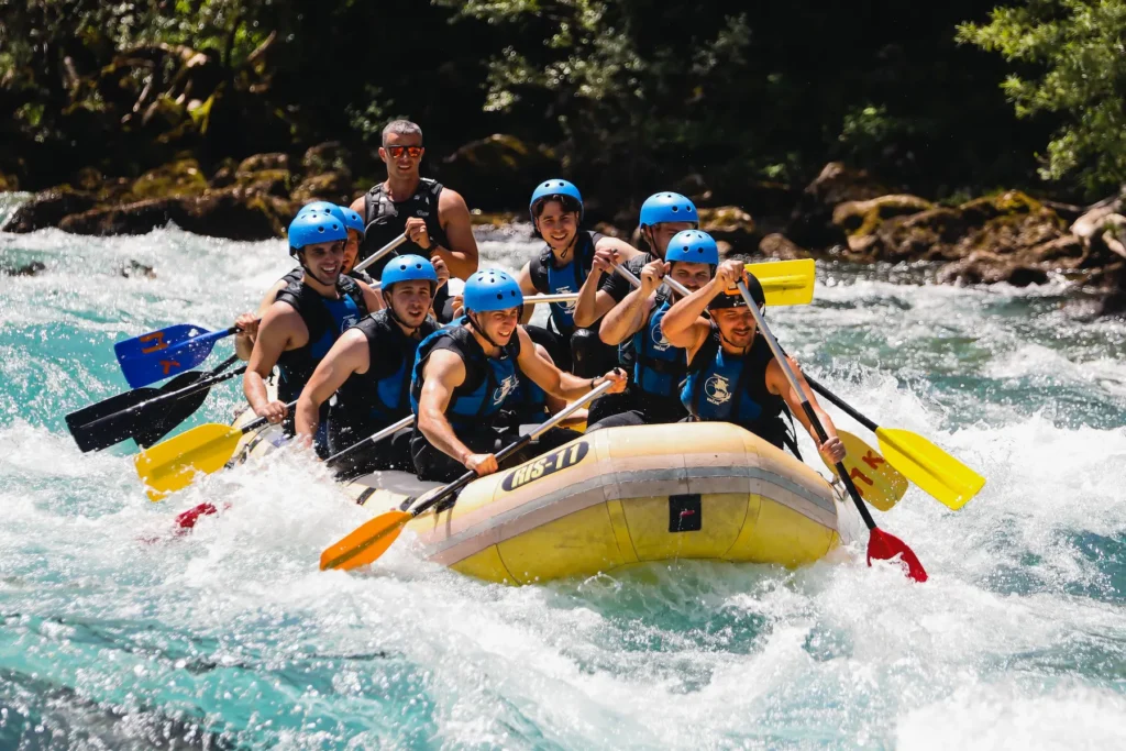 Naslovna Several individuals enjoying a rafting adventure on a river, with trees lining the banks in the background.