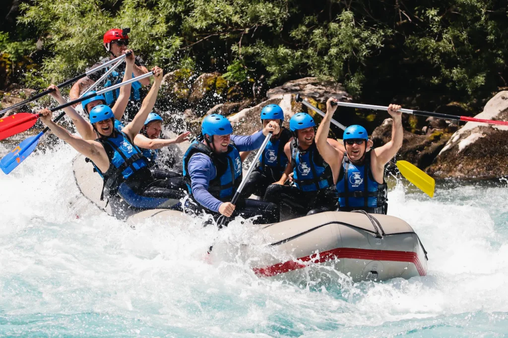 Naslovna A group of people joyfully rafting down a river, surrounded by lush greenery and clear blue skies.