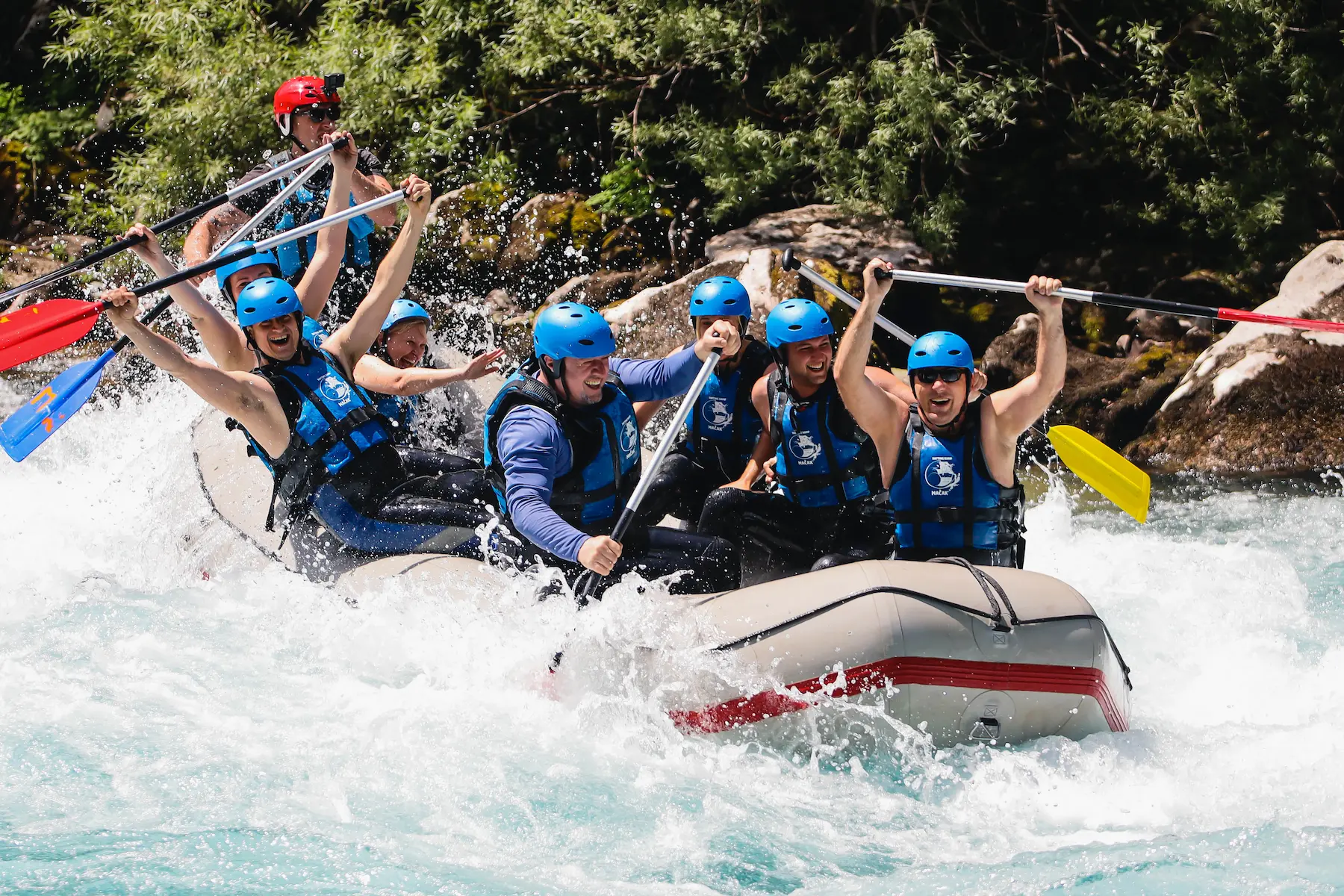 Naslovna A group of people joyfully rafting down a river, surrounded by lush greenery and clear blue skies.