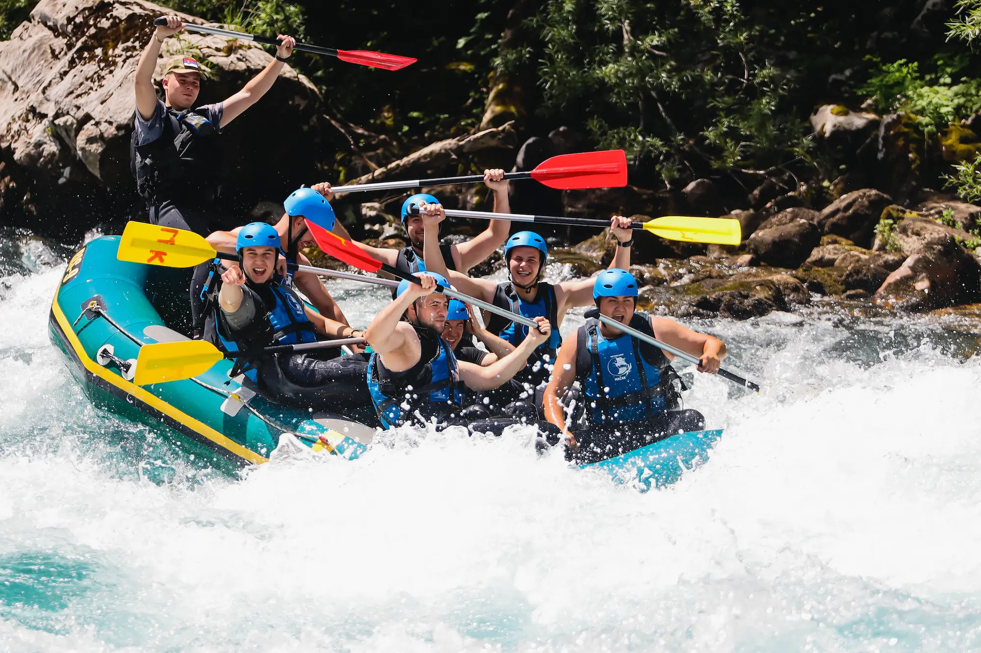Naslovna A diverse group of people navigating a river in a raft, showcasing teamwork and excitement amidst nature.