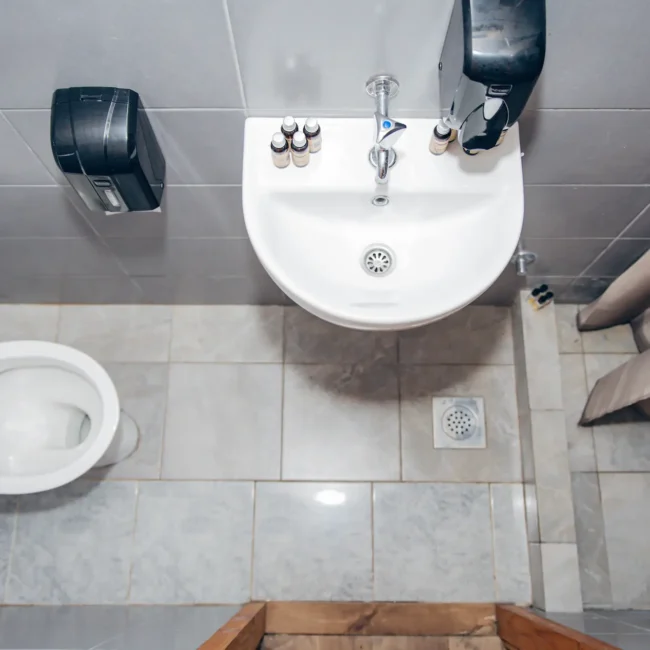 Top view of a bathroom featuring a white toilet and a small sink with a soap dispenser, tiled walls, and a shower curtain.
