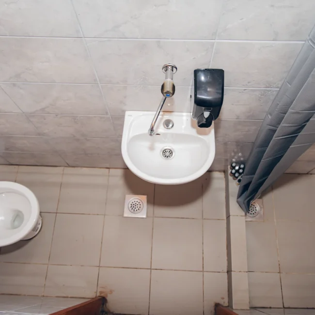 Top view of a bathroom featuring a white toilet and a small sink with a soap dispenser, tiled walls, and a shower curtain.