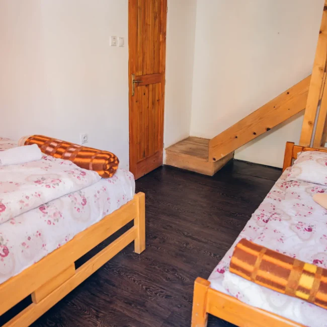 Cozy bedroom with two wooden beds, floral bedding, and a wooden staircase leading to an upper level.